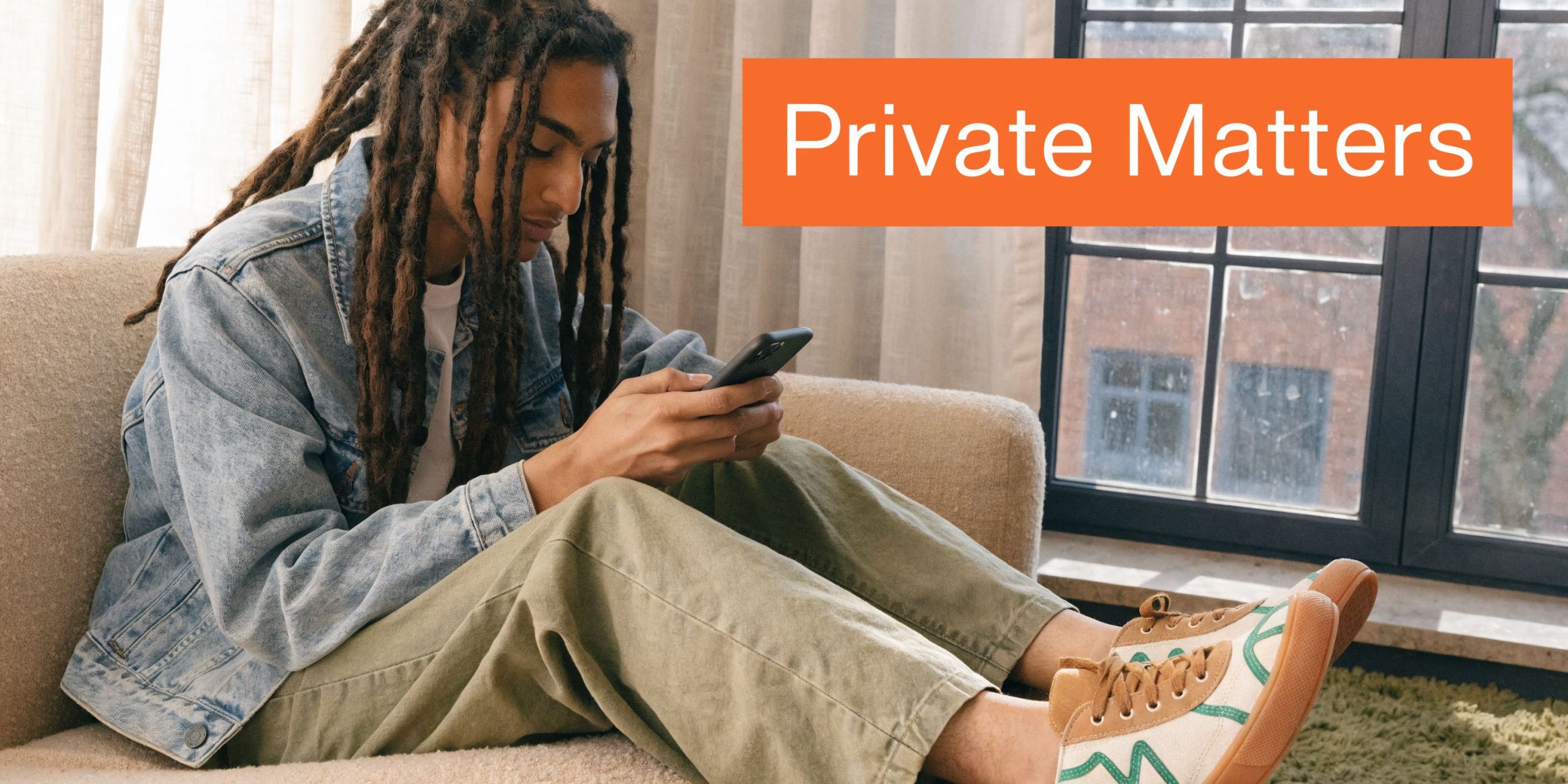 A young person with dreadlocks sitting on a couch and looking at a smartphone screen.