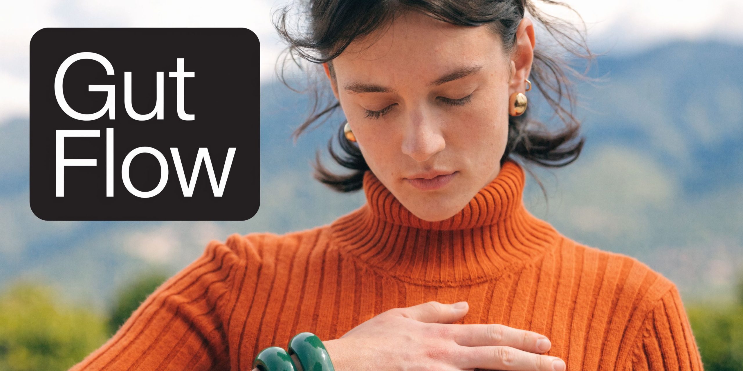 A person wearing a ribbed orange sweater resting their hand over their chest, suggesting gut health awareness.