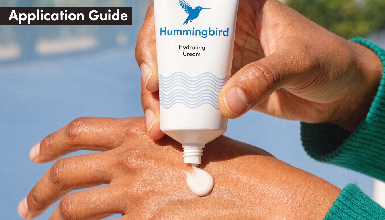 A person applying Hummingbird Hydrating Cream from a white tube onto the back of their hand.